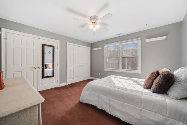 bedroom with ceiling fan, visible vents, baseboards, dark carpet, and two closets