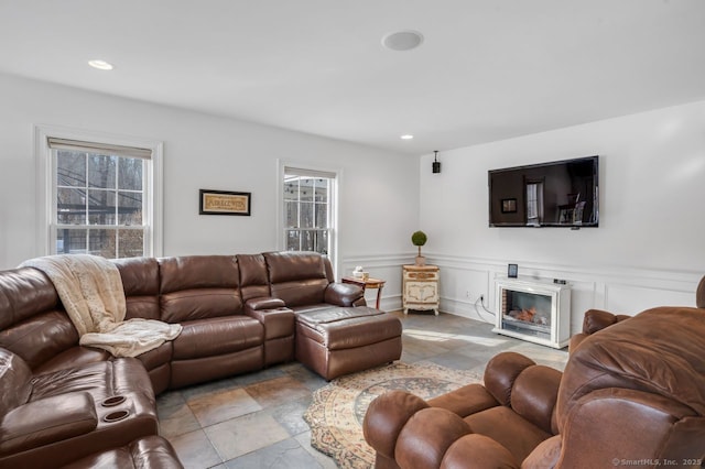 living area featuring wainscoting, recessed lighting, a decorative wall, and a glass covered fireplace