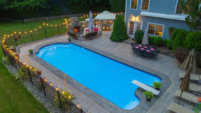 view of swimming pool featuring a fenced in pool, a patio area, a warm lit fireplace, and a fenced backyard