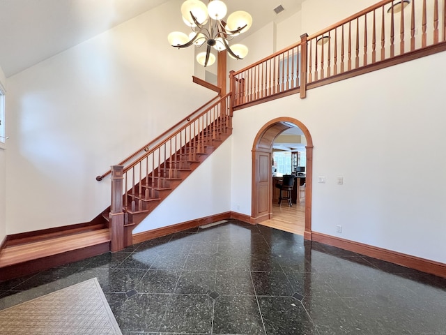 stairway featuring arched walkways, a notable chandelier, a high ceiling, granite finish floor, and baseboards