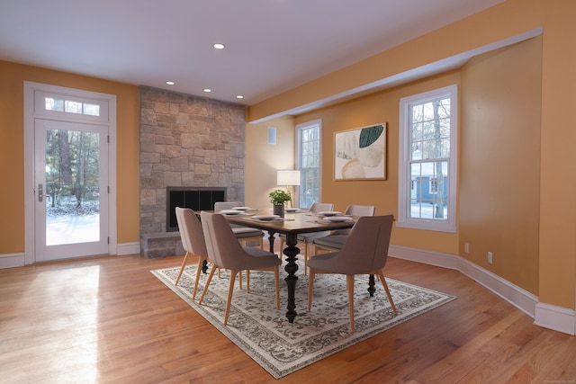 dining space with a stone fireplace, light wood finished floors, and baseboards