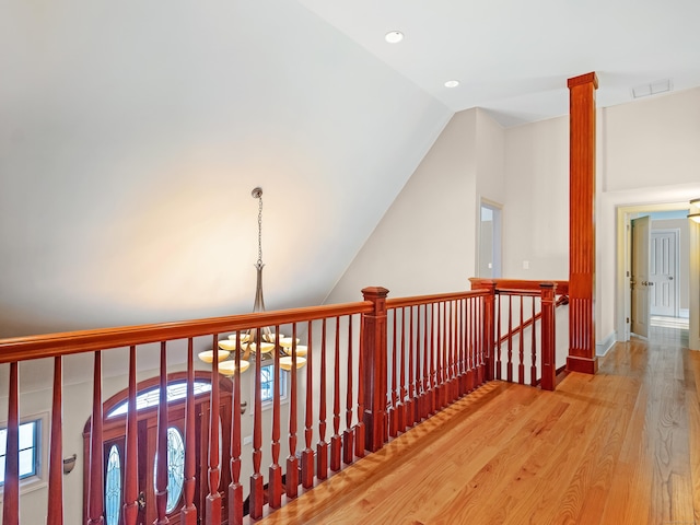 hall with a chandelier, wood finished floors, an upstairs landing, visible vents, and vaulted ceiling