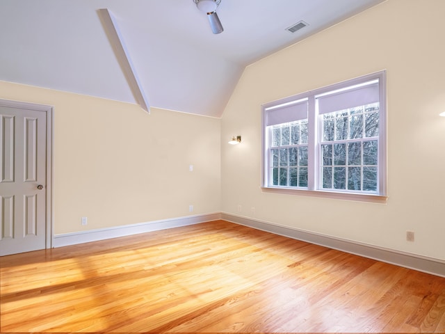 spare room featuring lofted ceiling, visible vents, baseboards, and wood finished floors