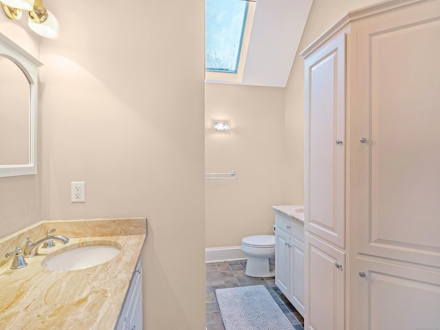 bathroom with toilet, lofted ceiling with skylight, vanity, and baseboards