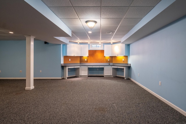 basement with a drop ceiling, dark carpet, and baseboards