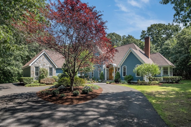 view of front facade with aphalt driveway, a front yard, stone siding, and a chimney