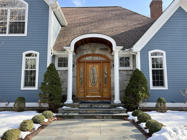 property entrance featuring stone siding, roof with shingles, and a chimney