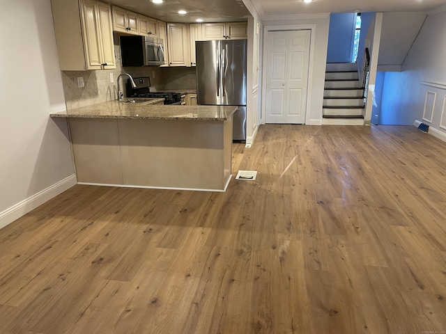 kitchen with light wood-style flooring, decorative backsplash, appliances with stainless steel finishes, light stone countertops, and baseboards