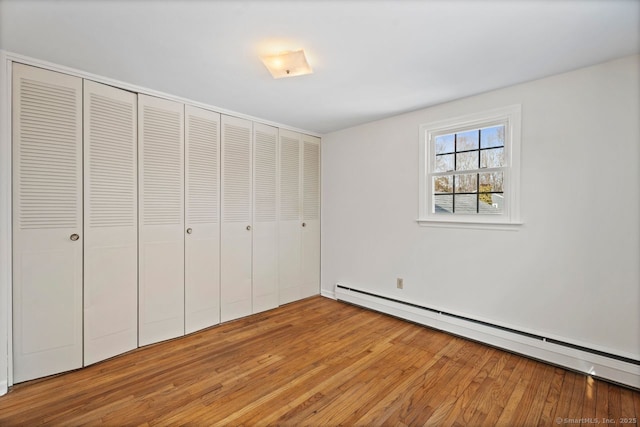 unfurnished bedroom with a closet, light wood finished floors, and baseboard heating