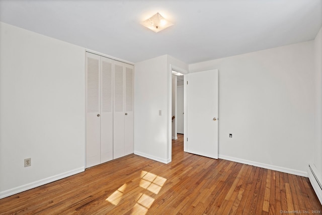 unfurnished bedroom featuring a closet, baseboard heating, wood-type flooring, and baseboards