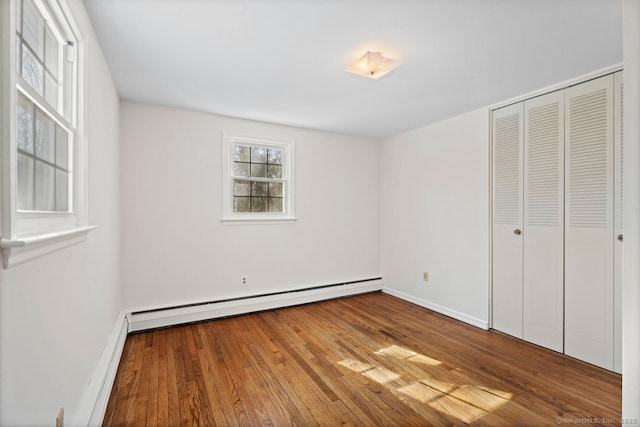 unfurnished bedroom featuring a baseboard radiator, a closet, baseboards, and wood finished floors