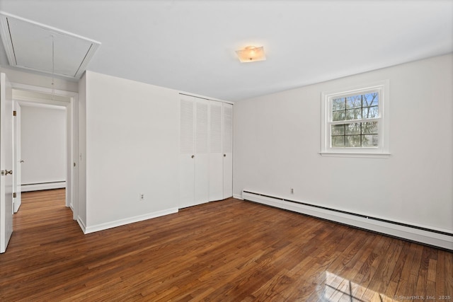 unfurnished bedroom featuring a baseboard radiator, attic access, and wood finished floors