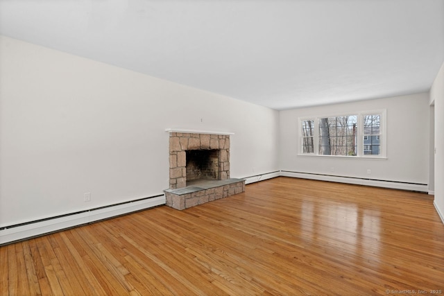 unfurnished living room with a baseboard radiator, hardwood / wood-style floors, and a stone fireplace