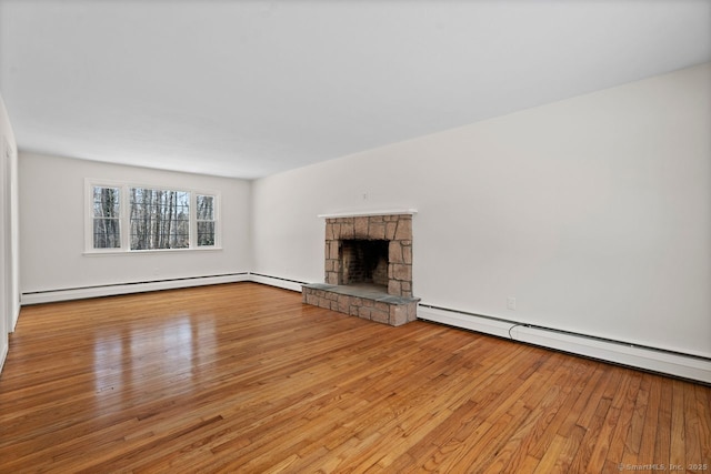 unfurnished living room with a baseboard heating unit, a stone fireplace, and hardwood / wood-style flooring