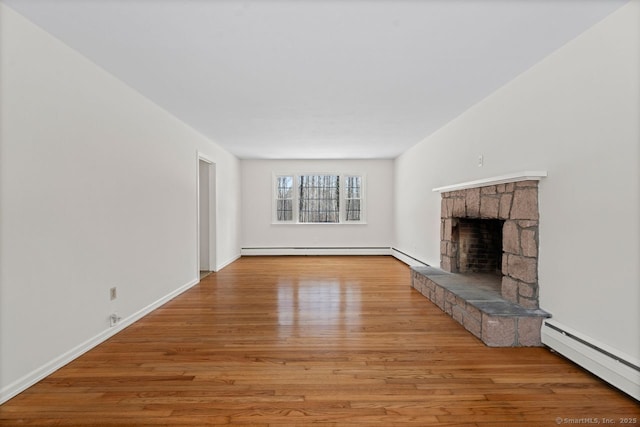 unfurnished living room with baseboards, baseboard heating, wood finished floors, and a stone fireplace