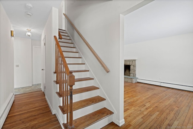 stairway with a baseboard heating unit, a fireplace, and wood finished floors