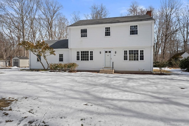 colonial inspired home with an outbuilding, a chimney, and a storage shed