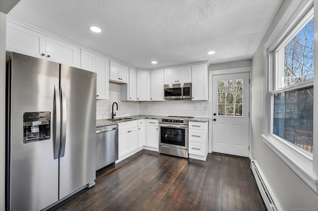 kitchen featuring a baseboard heating unit, stainless steel appliances, a sink, light stone countertops, and dark wood-style floors