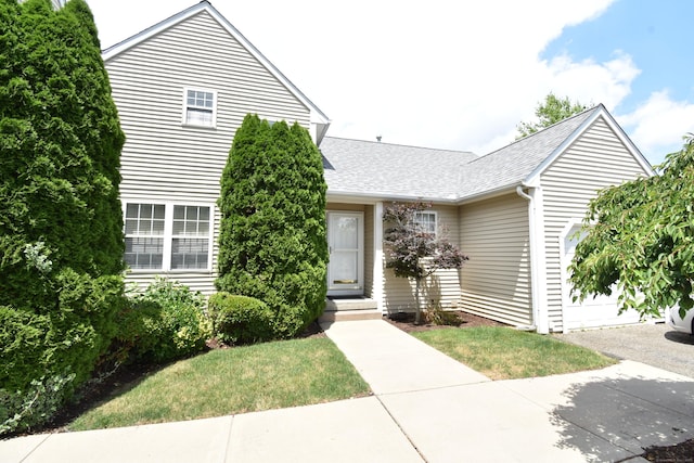 view of front facade with a garage, a shingled roof, and a front yard