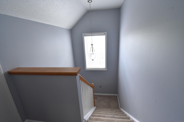 staircase featuring lofted ceiling, a textured ceiling, carpet, and baseboards