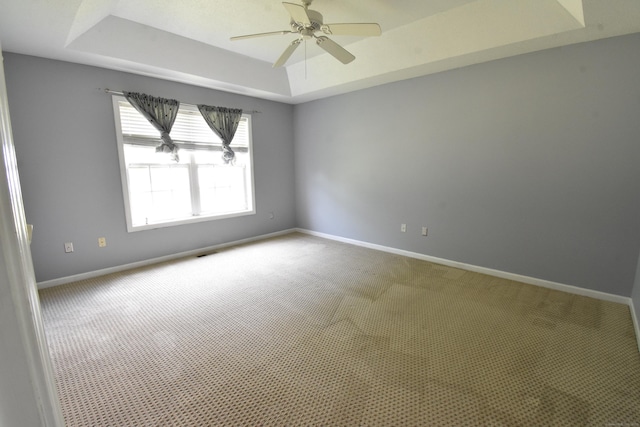 unfurnished room featuring a ceiling fan, a tray ceiling, carpet, and baseboards