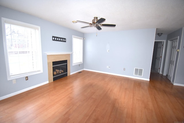 unfurnished living room with baseboards, visible vents, wood finished floors, and a glass covered fireplace