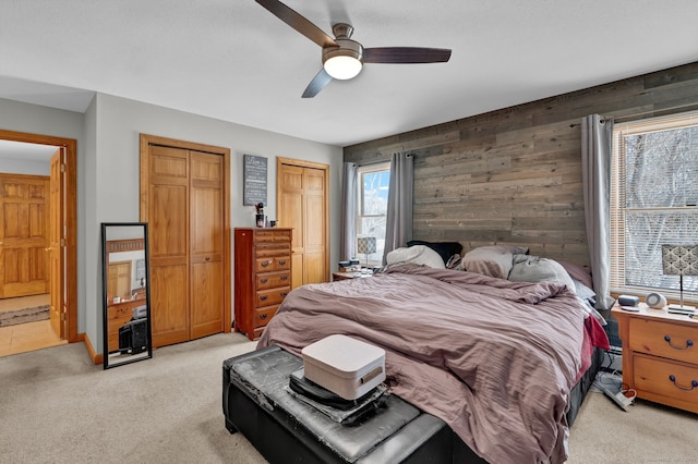 bedroom with light carpet, two closets, a ceiling fan, and wooden walls