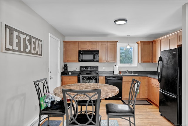 kitchen with a sink, light wood-type flooring, black appliances, dark countertops, and pendant lighting