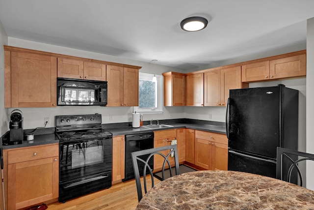 kitchen with black appliances, dark countertops, a sink, and light wood-style flooring