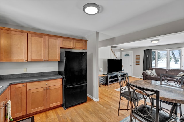 kitchen with dark countertops, light wood-style floors, freestanding refrigerator, open floor plan, and baseboards