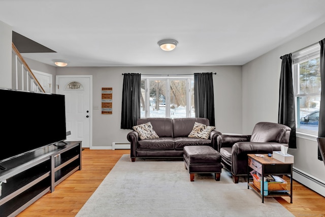 living room with stairs, light wood finished floors, a baseboard radiator, and baseboards