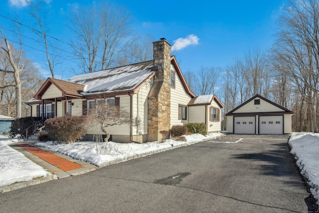 view of snowy exterior with a garage, an outbuilding, and a chimney