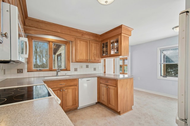 kitchen with light countertops, backsplash, a sink, white appliances, and a peninsula