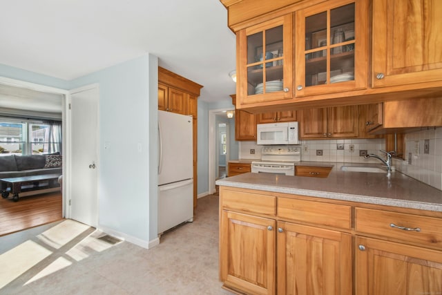 kitchen featuring white appliances, tasteful backsplash, brown cabinetry, glass insert cabinets, and a sink