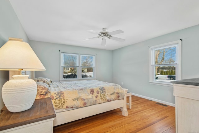 bedroom with a ceiling fan, visible vents, baseboards, and wood finished floors