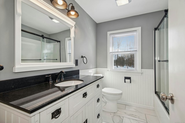 full bathroom featuring marble finish floor, toilet, wainscoting, combined bath / shower with glass door, and vanity