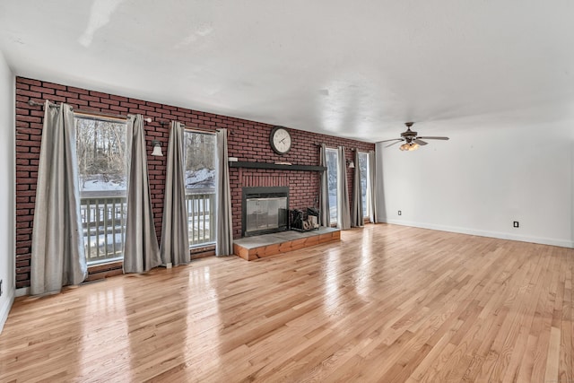 unfurnished living room featuring a brick fireplace, a ceiling fan, baseboards, and wood finished floors