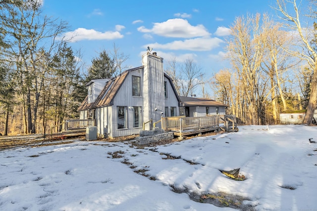 snow covered property featuring central air condition unit, a chimney, and a wooden deck