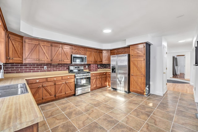 kitchen with appliances with stainless steel finishes, brown cabinets, a sink, and light countertops