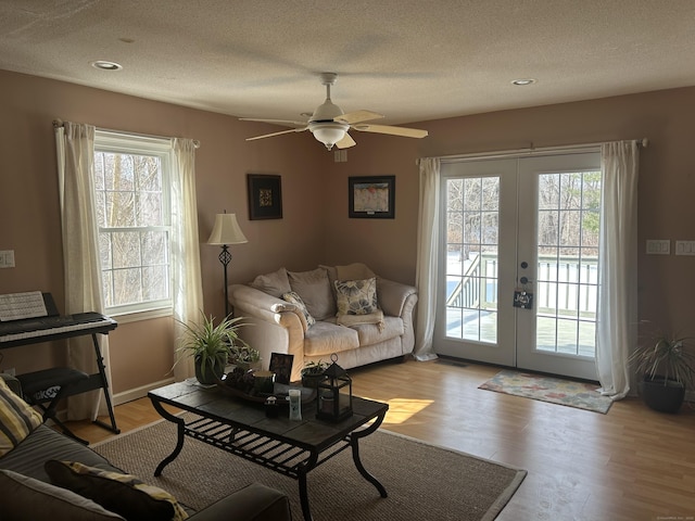 living area with light wood-type flooring, french doors, a textured ceiling, and baseboards