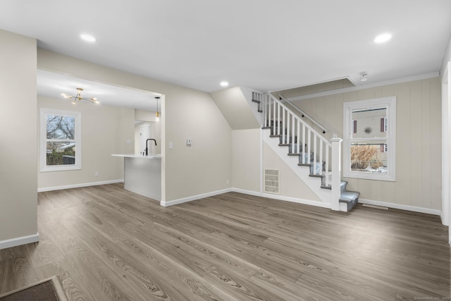 unfurnished living room featuring a sink, wood finished floors, visible vents, baseboards, and stairway