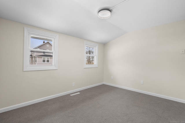 empty room featuring lofted ceiling, carpet floors, visible vents, and baseboards