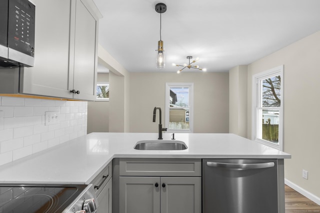 kitchen with gray cabinetry, stainless steel appliances, a sink, light countertops, and tasteful backsplash