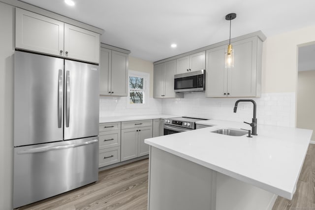 kitchen featuring pendant lighting, gray cabinets, light countertops, appliances with stainless steel finishes, and a sink