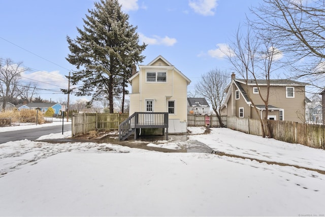 snow covered rear of property featuring a residential view, fence, and a deck