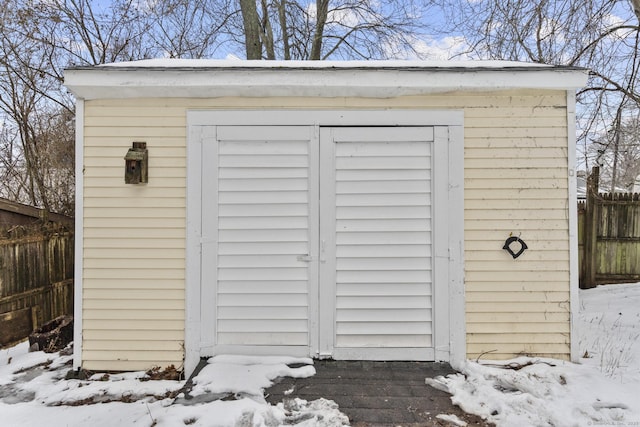 snow covered structure with a shed, fence, and an outdoor structure