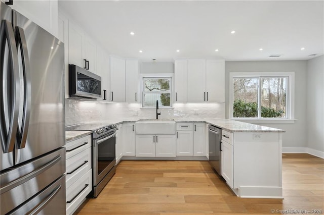 kitchen with a peninsula, a sink, appliances with stainless steel finishes, light wood-type flooring, and tasteful backsplash