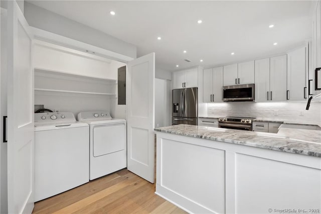 kitchen with stainless steel appliances, light wood-style floors, white cabinetry, light stone countertops, and washer and dryer