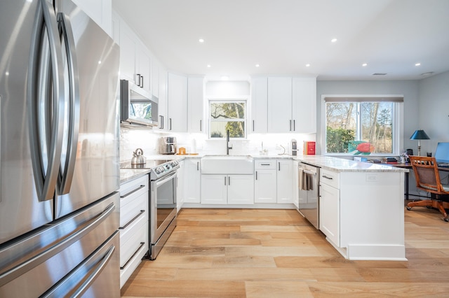 kitchen featuring a peninsula, light wood-type flooring, appliances with stainless steel finishes, and a sink