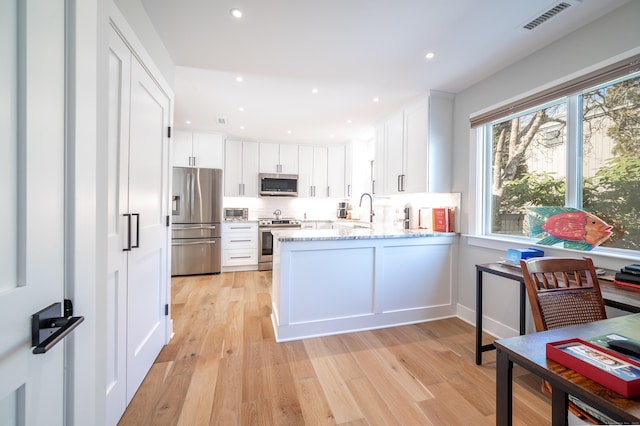 kitchen with a peninsula, a sink, visible vents, white cabinetry, and appliances with stainless steel finishes